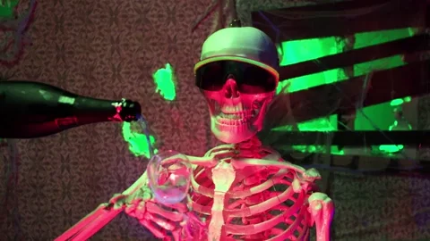 A gif of a skeleton wearing sunglasses and a cap while holding an empty glass. Champagne is poured into the glass and the skeleton flips it up, causing the liquid to go everywhere.